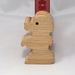 May include: A wooden toy shaped like a standing bear. The bear is light brown and has a hole in its head. The bear is about 4 inches tall.