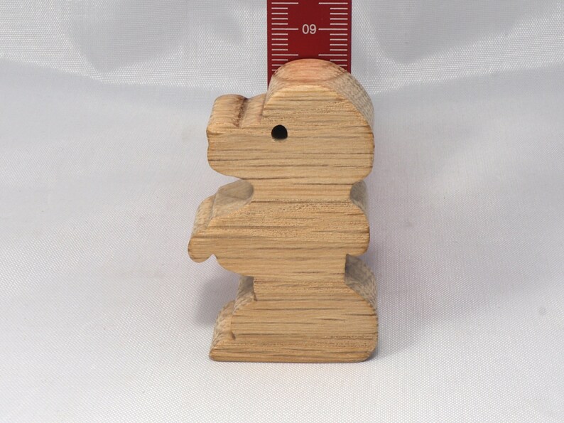 May include: A wooden toy shaped like a standing bear. The bear is light brown and has a hole in its head. The bear is about 4 inches tall.