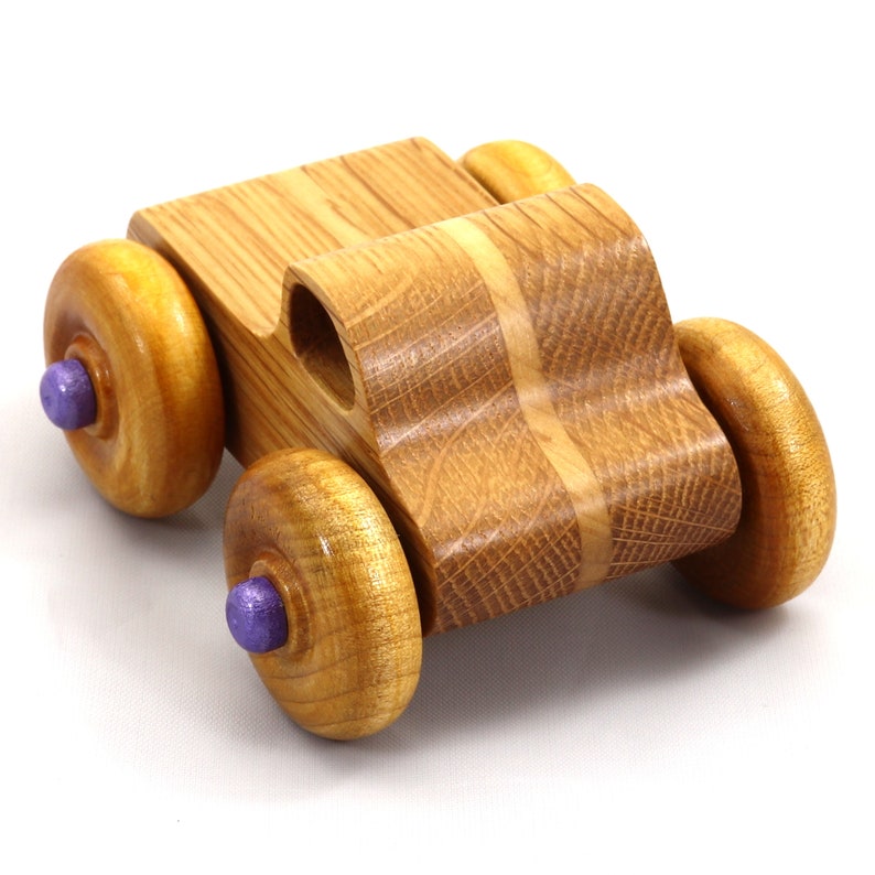 May include: A handcrafted wooden toy car with a natural wood finish. The car features four large, round wheels with purple center accents. The body of the car is made of light brown wood with a curved design.