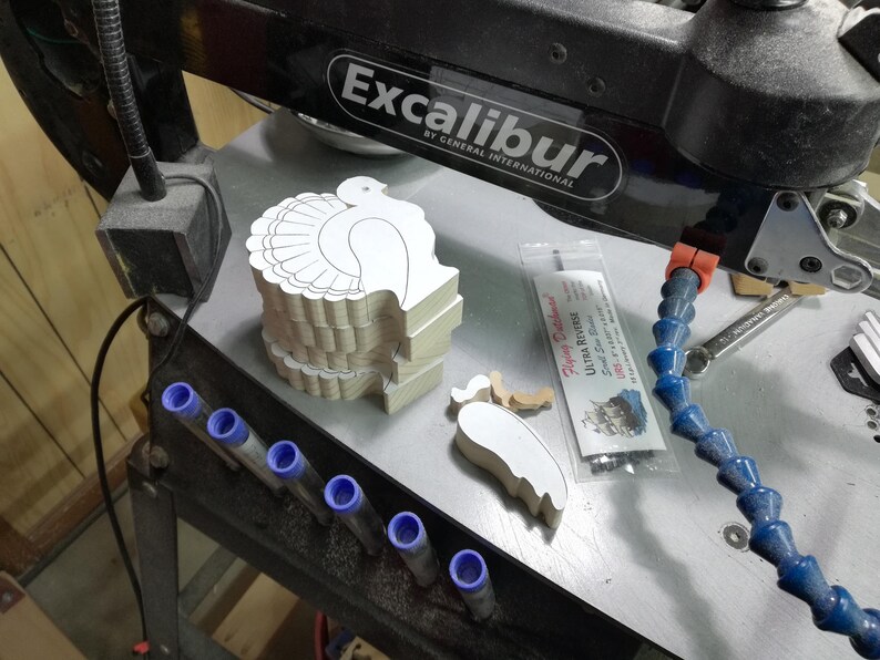 Stacked unfinished wooden turkey shapes and separate wing pieces on my Excabur Ex-21 scroll saw in the workshop.