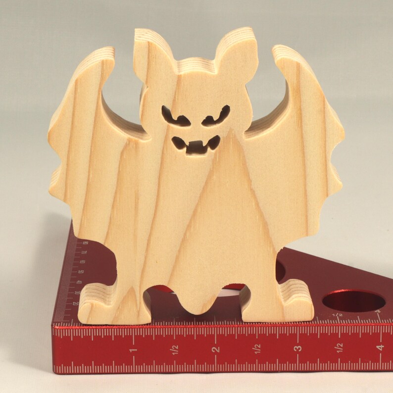 Handmade unpainted wooden Halloween bat cutout, freestanding light-colored solid wood figure with spooky carved face and outstretched wings, ready to paint, from my Snazzy Spooks collection. Standing on a ruler.