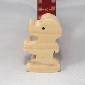 May include: A wooden figurine of a person standing with arms outstretched. The figurine is made of light brown wood and is about 4 inches tall.