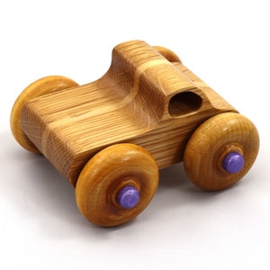 May include: A handcrafted wooden toy car with a natural wood finish. The car features four round wheels with purple center accents. The body of the car is carved with smooth lines and a small opening. A classic toy for children.
