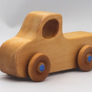 Wooden toy pickup truck from the Play Pal Collection at Odin's Toy Factory. Made from natural wood, finished with amber shellac, and accented with metallic sapphire blue acrylic paint on the wheel hubs. Made In The USA. Approximate dimensions: length 3-1/2 inches, height 1-3/8 inches, width 1-1/2 inches, wheels 3/4 inch diameter. Handmade in Tallahassee, Florida. Natural wood grain and color variations.
