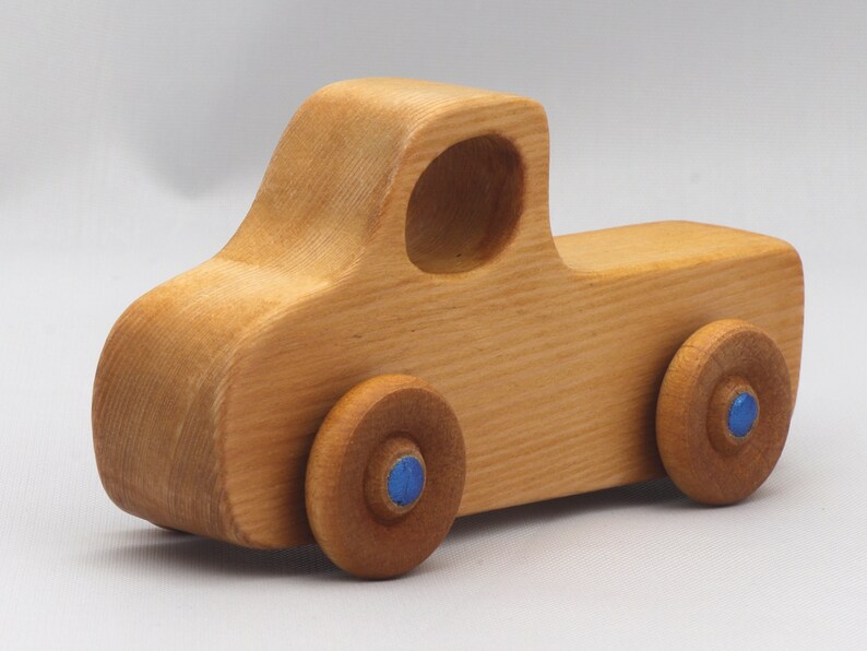 Wooden toy pickup truck from the Play Pal Collection at Odin's Toy Factory. Made from natural wood, finished with amber shellac, and accented with metallic sapphire blue acrylic paint on the wheel hubs. Made In The USA. Approximate dimensions: length 3-1/2 inches, height 1-3/8 inches, width 1-1/2 inches, wheels 3/4 inch diameter. Handmade in Tallahassee, Florida. Natural wood grain and color variations.