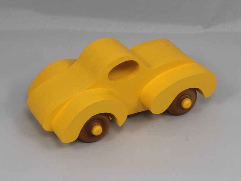 Handmade wooden toy car vintage style of a fat fendered coupe painted bright yellow with nonmarring amber shellac finished wheels. It is an excellent push toy for a younger child.