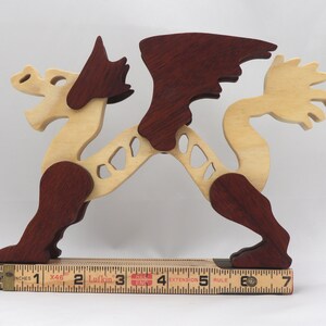Handmade wooden dragon figurine. crafted from contrasting hardwoods with a light natural wood body and head paired with rich dark reddish-brown wings, legs, and horns. Displayed on a folding carpenters rule for scale.