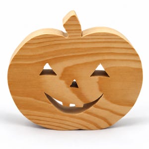 Handmade unpainted wooden Jack-o-Lantern cutout with carved triangular eyes, nose, smiling mouth, and stem, shown freestanding on a white background. Ready to paint for Halloween decoration.