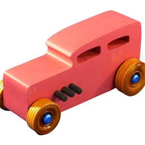 Handcrafted pink wooden hot rod '32 sedan toy car. Features black and metallic sapphire blue accents, and non-marking amber shellac wheels. Made to order for unique play or display.