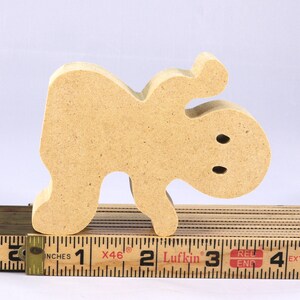 A handmade, unpainted wooden ghost cutout stands upright on a white background. The light-colored solid wood figure has a rounded head with two circular eye cutouts, raised wavy arms, and a curved wavy base, ready for painting or crafting.