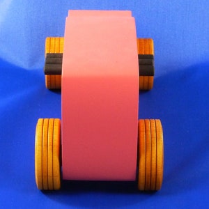 Handcrafted pink wooden hot rod '32 sedan toy car. Features black and metallic sapphire blue accents, and non-marking amber shellac wheels. Made to order for unique play or display.