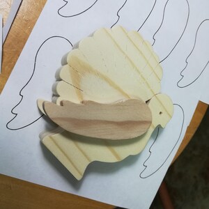Unfinished wooden turkey with a contrasting wood wing resting on printed wing patterns during assembly.