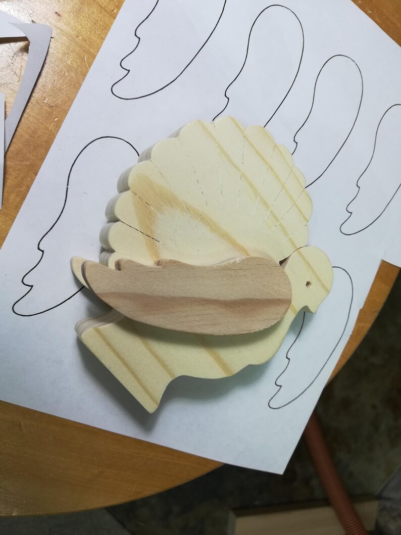 Unfinished wooden turkey with a contrasting wood wing resting on printed wing patterns during assembly.
