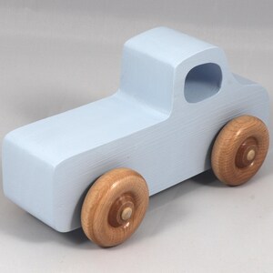 May include: A light blue wooden toy truck with natural wood wheels. The truck has a simple, blocky design with a cab and a cargo bed. The wheels are round and attached to the truck's body.