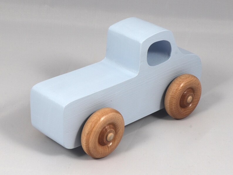 May include: A light blue wooden toy truck with natural wood wheels. The truck has a simple, blocky design with a cab and a cargo bed. The wheels are round and attached to the truck's body.