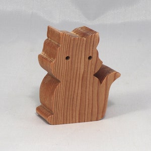 May include: A wooden toy squirrel figurine with a light brown finish. The squirrel is standing on its hind legs with its tail curled behind it.