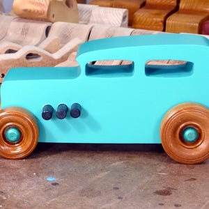 Handmade wooden toy car, 1932 Hot Rod Sedan, painted turquoise with metallic green and black trim. The wheels are finished with nonmarring amber shellac. Handcrafted from natural wood in Tallahassee, Florida, USA. Approximate size: 6 inches long, 3 inches high, 2.5 inches wide. Odin's Toy Factory custom wooden toy.