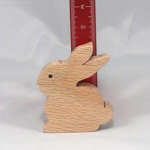 May include: A wooden rabbit figurine, approximately 3 inches tall, with a natural wood finish. The rabbit is sitting upright with its ears perked up.