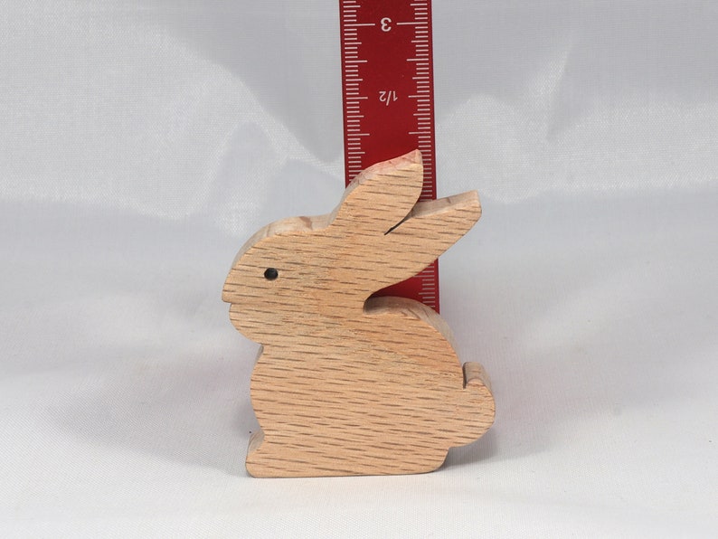 May include: A wooden rabbit figurine, approximately 3 inches tall, with a natural wood finish. The rabbit is sitting upright with its ears perked up.