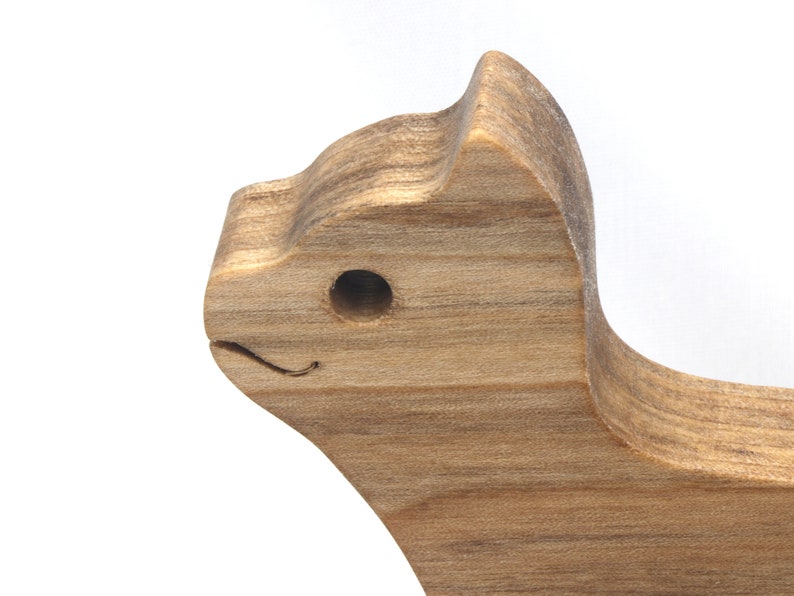 A freestanding wooden puzzle cut in the shape of a large cat standing on four legs. Two smaller kitten figures nest on the large cat’s back and interlock as puzzle pieces. Simple drilled holes form the eyes and nose on each cat, with a shallow cut line for the mouth on the large cat. The completed puzzle stands upright on a plain white surface. Handmade by Odin’s Toy Factory In Tallahassee, Florida, USA.
