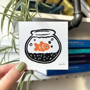 May include: A black and white illustration of a fishbowl with an orange goldfish inside. The fishbowl is filled with black dots and bubbles.