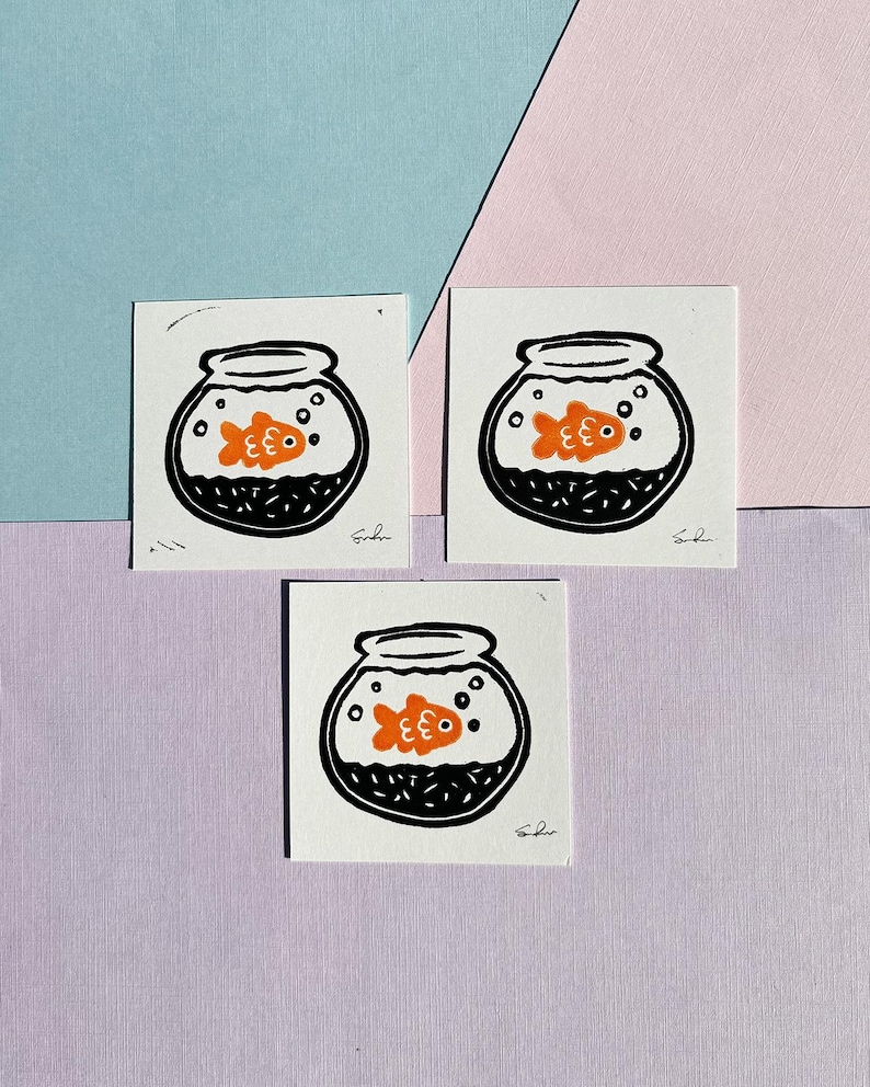May include: Three black and white illustrations of a goldfish in a bowl. The goldfish is orange and has a black eye. The bowl is filled with black and white dots to represent water.