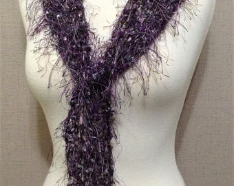 May include: A purple and white fuzzy scarf with a long fringe. The scarf is tied in a knot around a white mannequin.