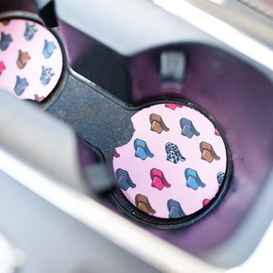 May include: Two pink and black car cup coasters with a pattern of colorful cowboy hats.