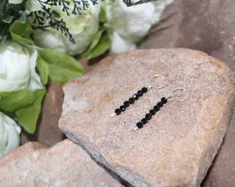 May include: A pair of dangle earrings with black beads and silver hoops.