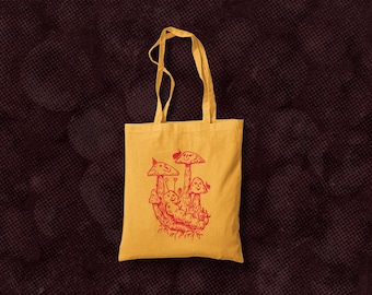 Puede incluir: Una bolsa de tela amarilla con una ilustración roja de setas. Las setas tienen caras sonrientes y están agrupadas.