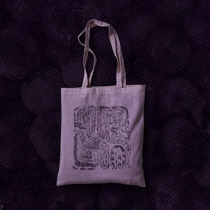 Może przedstawiać: Biała torba typu tote z czarnym atramentowym rysunkiem labiryntu z stworzeniem w środku. Torba typu tote ma dwa uchwyty.