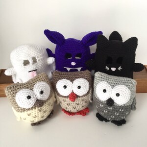 May include: Five crocheted Halloween-themed plush toys: a ghost, a bat, a black cat, and two owls. One owl is brown with red accents, and the other is grey.