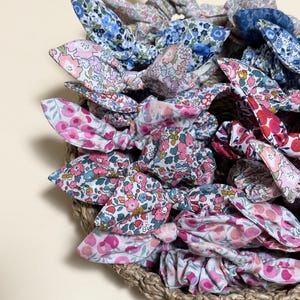 May include: A collection of floral patterned hair bows in a woven basket. The bows feature various colors, including pink, blue, and red, with delicate floral designs. The basket is made of natural woven material.