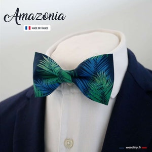 Könnte beinhalten: Eine marineblaue Fliege mit einem tropischen Blattmuster in Grün- und Blautönen. Die Fliege ist geknotet und wird mit einem weißen Hemd mit Kragen und einem marineblauen Blazer getragen. Der Text "Amazonia" befindet sich über der Fliege.