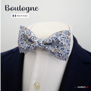 Peut inclure: Un nœud papillon à motifs floraux dans les tons de bleu, blanc et marron, porté avec une chemise blanche et un blazer bleu marine. Le nœud papillon est orné d'un motif floral délicat. Le texte "Boulogne" est visible en haut.