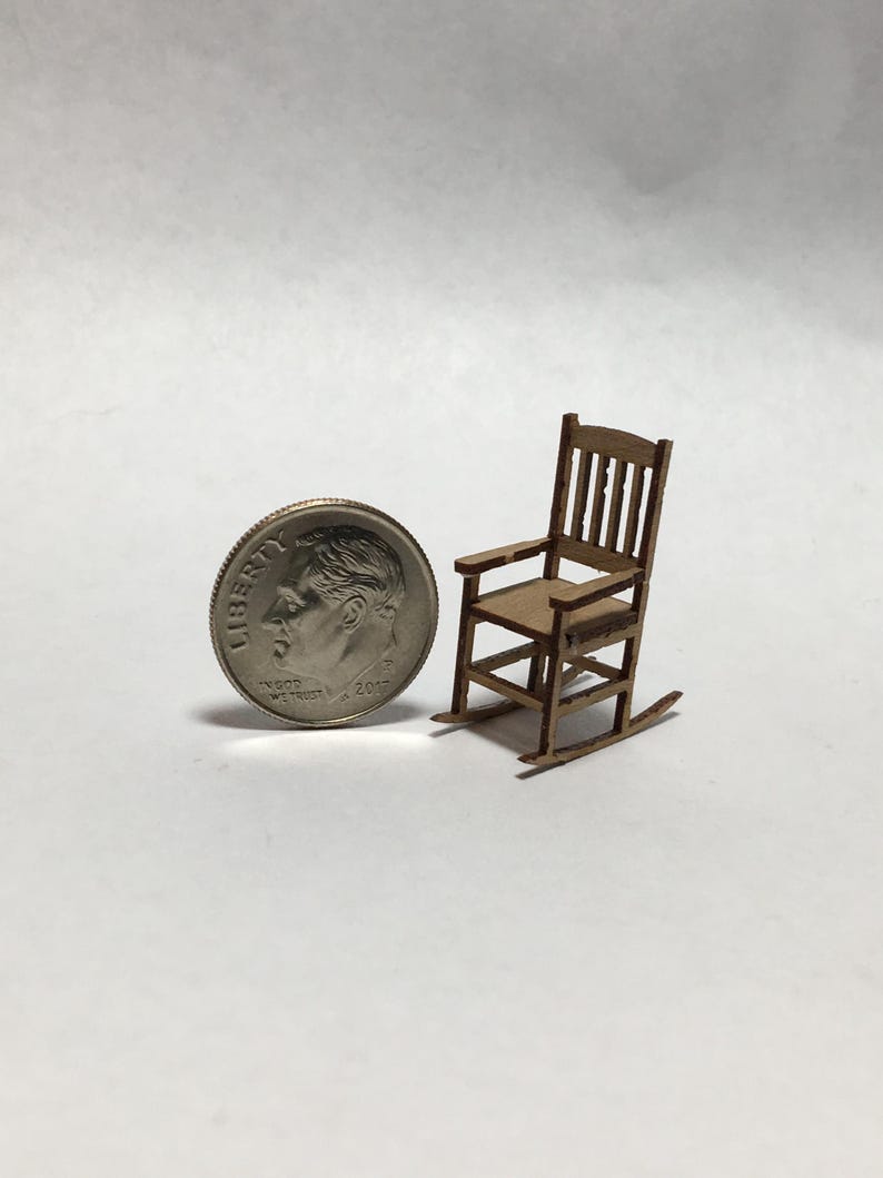 May include: Miniature wooden rocking chair with a light brown finish. The chair has a slatted back and armrests. A U.S. dime is next to the chair for scale. The chair is a small-scale model.