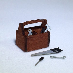 Peut inclure: Une boîte à outils en bois avec une finition brune et une poignée en métal. La boîte à outils est ouverte et contient une variété d'outils, dont une scie, une clé et un marteau.