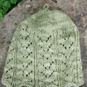 May include: A green knitted hat with a lacy pattern. The hat has a small loop at the top.