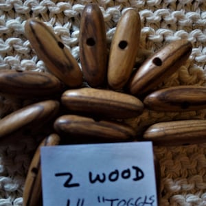 May include: A close-up of 12 wooden toggles with a handwritten note that says "2 wood 1 1/2" toggles".
