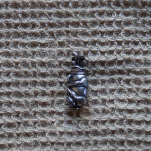 May include: A silver golf bag charm with a detailed design. The charm is small and would be a great addition to a golf bag or keychain.