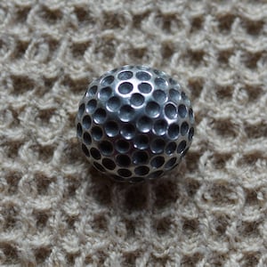 May include: A silver golf ball with dimples.