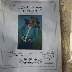 May include: A knitting kit from North Island Designs, featuring a photo of a child wearing a teal sweater. The kit includes yarn and instructions for sizes 4-8. Rolls of white and blue yarn are visible.