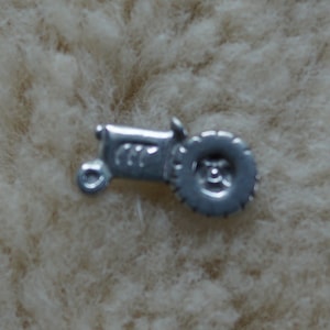 May include: A silver charm in the shape of a tractor with a single large wheel. The tractor is facing to the right.