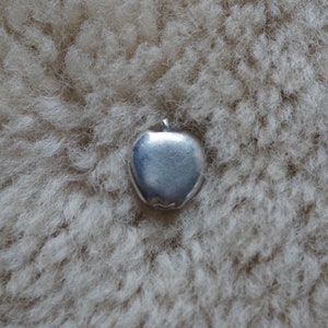 May include: A silver charm in the shape of an apple. The charm is smooth and shiny.