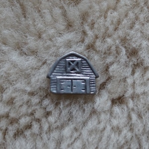 May include: A silver metal barn charm with a single window and a closed door. The charm is small and would be suitable for a keychain or a scrapbook.