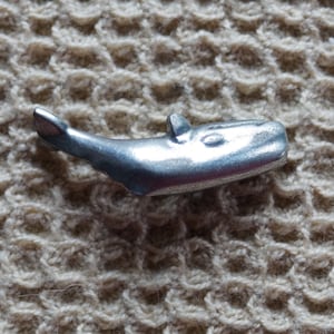 May include: A silver whale figurine, a game piece for a board game.