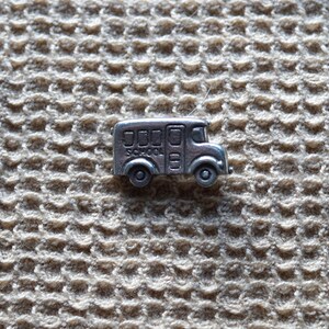 May include: A small, silver-toned metal charm shaped like a school bus. The side of the bus features embossed windows, a door, and the word SCHOOL printed in capital letters. The charm has two wheels and a rounded front hood design.