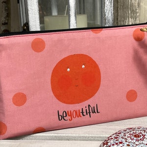 Könnte beinhalten: Rosa durchsichtige Tasche mit einem roten Kreis-Gesicht und dem Text "be youtiful" in Schwarz. Die Tasche hat ein Punkte-Muster mit roten Punkten auf rosa Hintergrund.