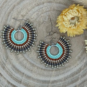 May include: A pair of beaded hoop earrings with a turquoise, brown, and gray color scheme. The earrings are made with small beads and have a silver hoop.