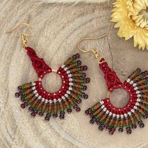 Könnte beinhalten: Ein Paar handgefertigte Ohrringe in Rot, Weiß, Braun und Grün. Die Ohrringe sind in Macrame-Technik gefertigt und haben ein kreisförmiges Design mit Perlen.